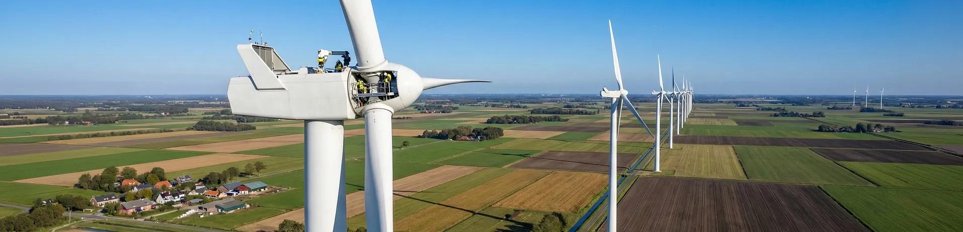 I line of white wind turbines in the middle of agricultural fields set against a blue sky