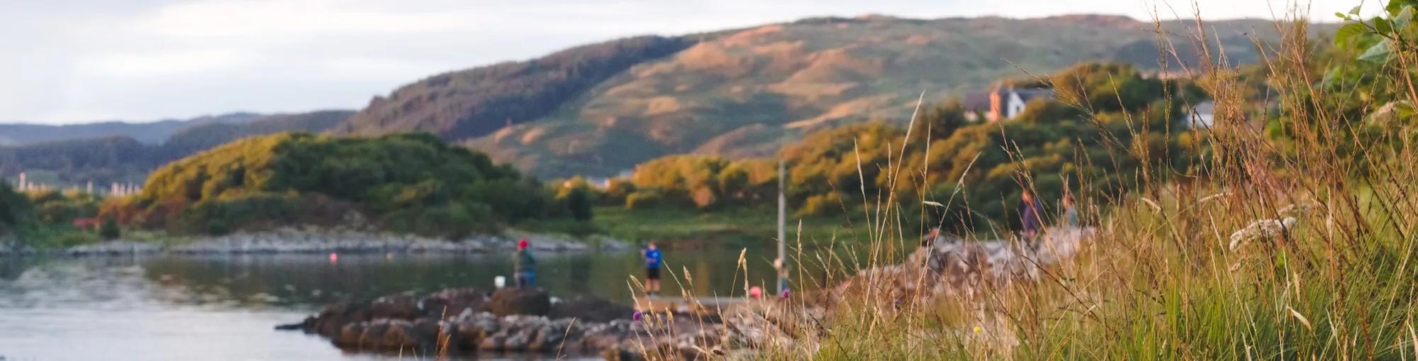 A scenic viw of a lake with mountains in the background. A family is playing on the rocks by the lake