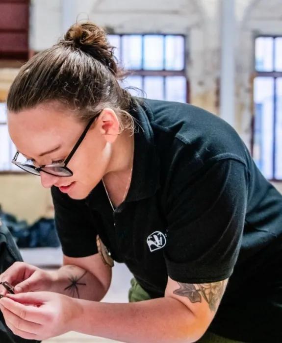 A woman in a dark green Wildlife Trust t-shirt crouches over a table looking at something in her hand
