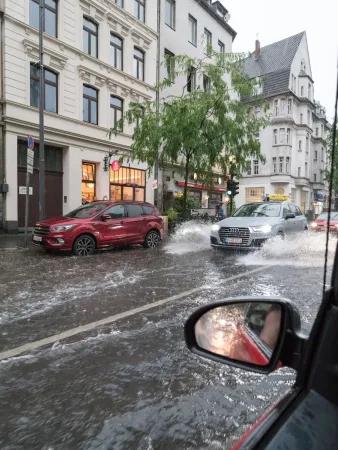 A city street with cars and shops which has been flooded. Photo is taken from the open window of a car
