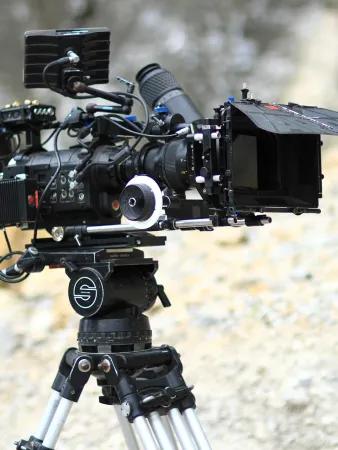 A film camera on a tripod outdoors in front of loose rock